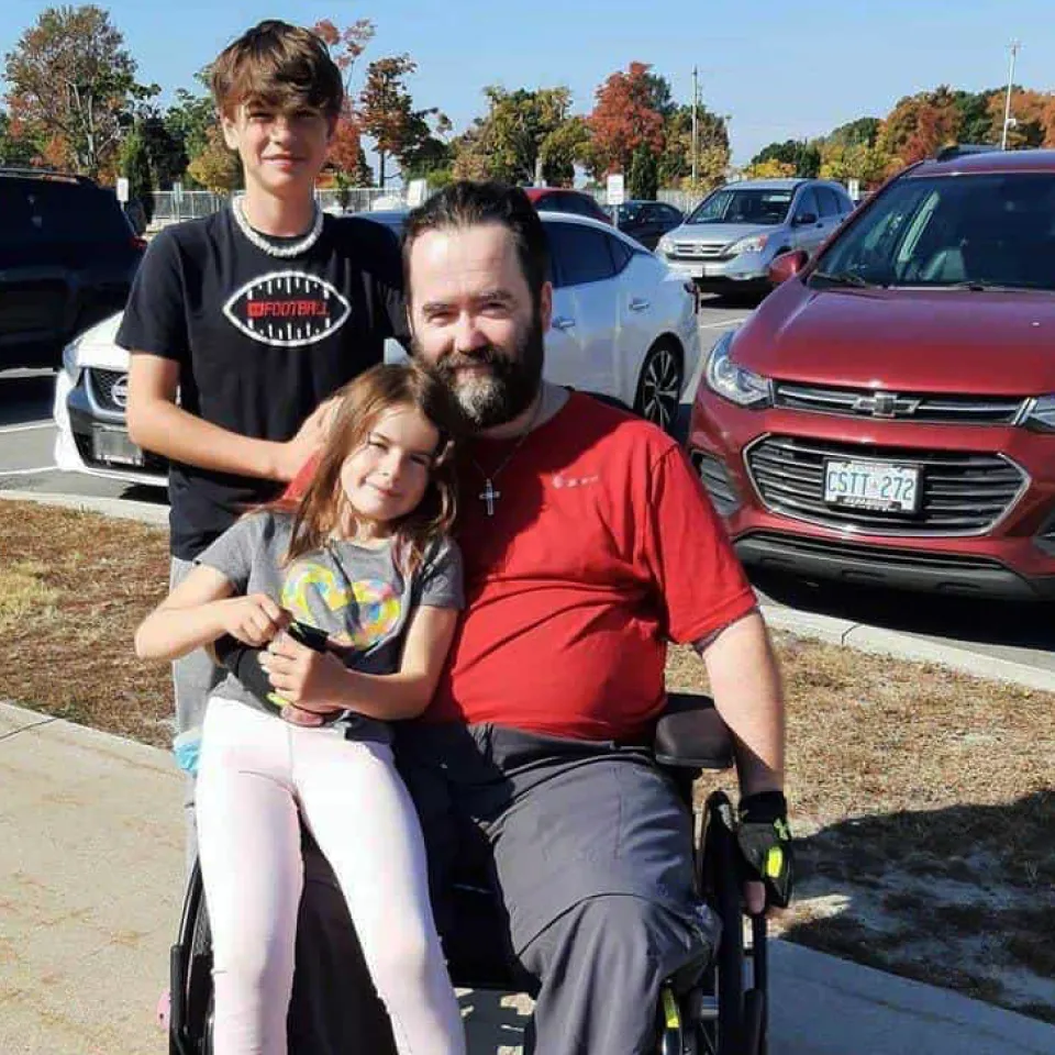 Corey Dunn sitting in a wheelchair being hugged by his family.